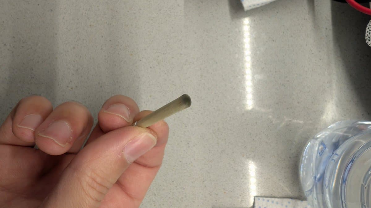 Hand holding fiberglass pen near CRT tube pins during oxidation cleaning with IPA and Deoxit on workbench.