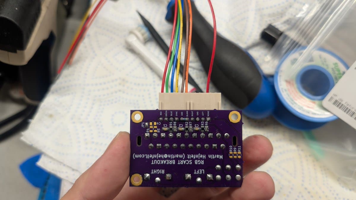 Purple SCART breakout PCB with multicolored ribbon cable connector, held in hand during RGB mod assembly for PVM-14L1.