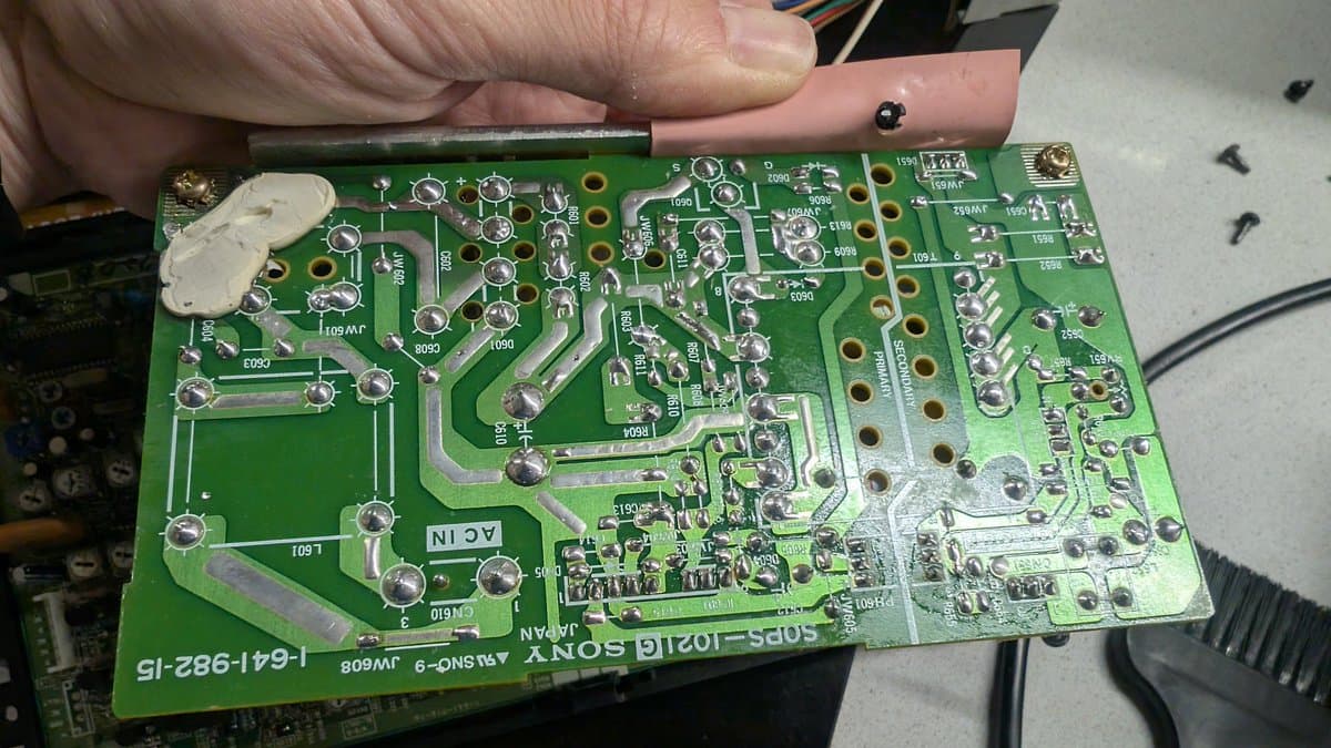 Sony PVM-6041Q PSU board with old capacitors and reflowed solder joints during restoration; hand holding screwdriver.