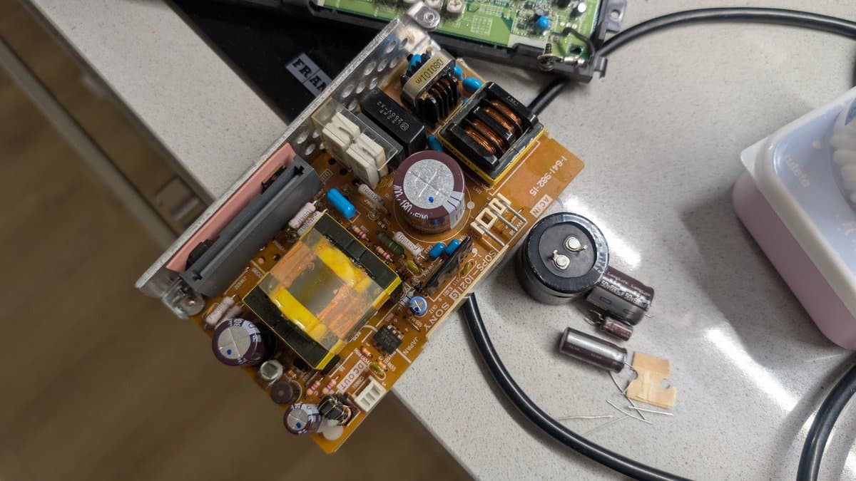 Disassembled Sony PVM-6041Q power supply board on workbench showing capacitors, transformers, and disconnected components during restoration.