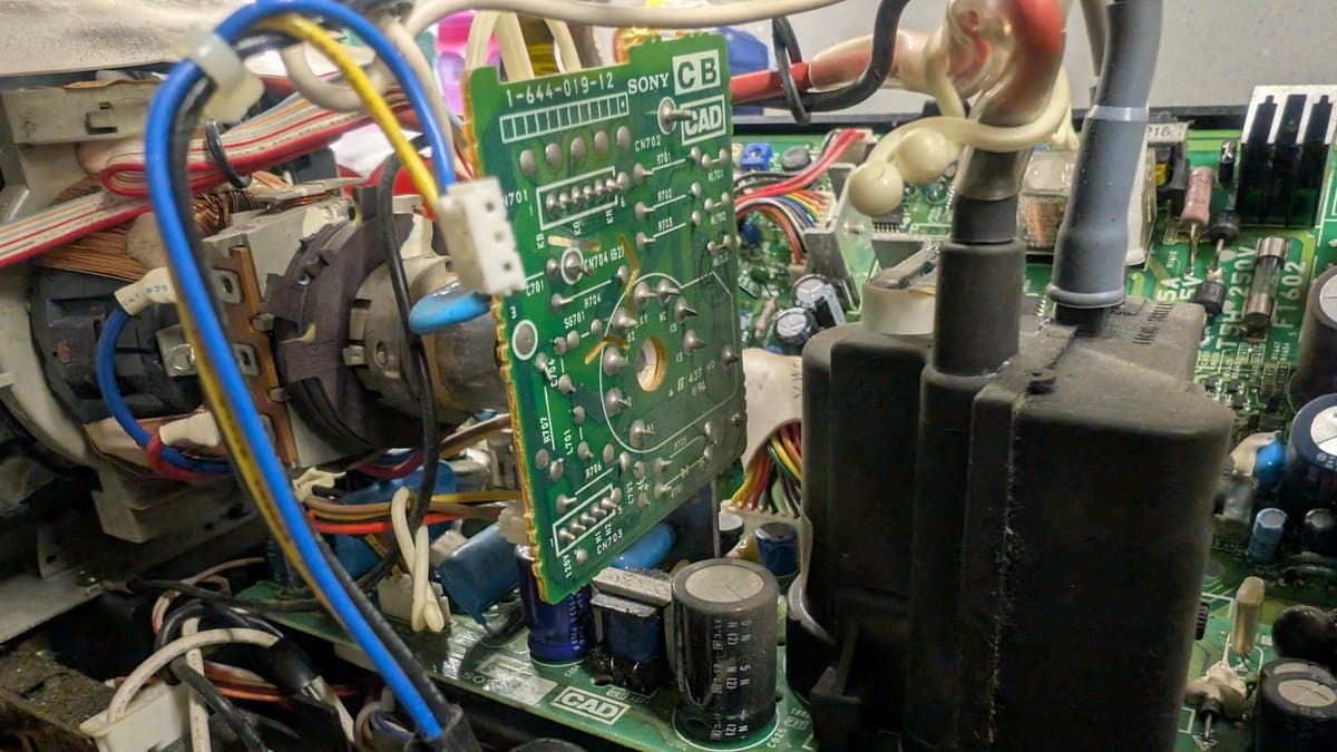 Interior of Sony PVM-6041Q showing dusty green circuit boards, capacitors, wiring harnesses, and black cylindrical components during restoration cleaning.