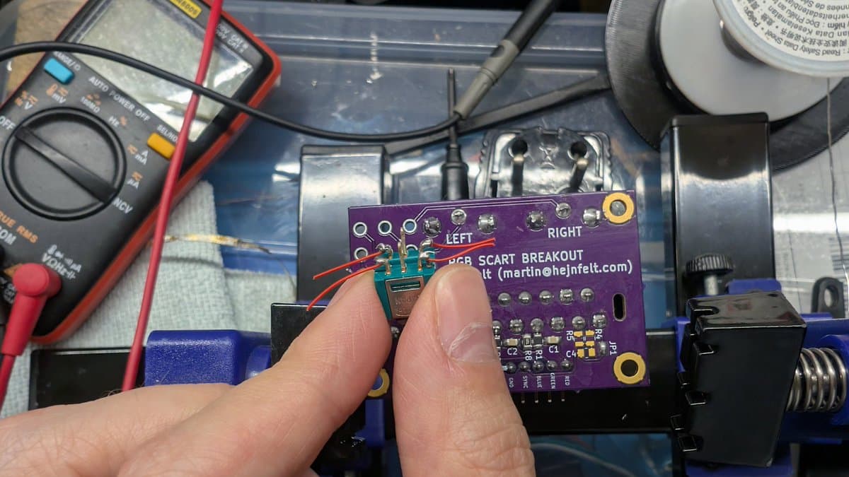 Hand holding RGB Scart Breakout PCB during assembly, showing soldered connections and bent pins for PVM-14L1 mod installation.