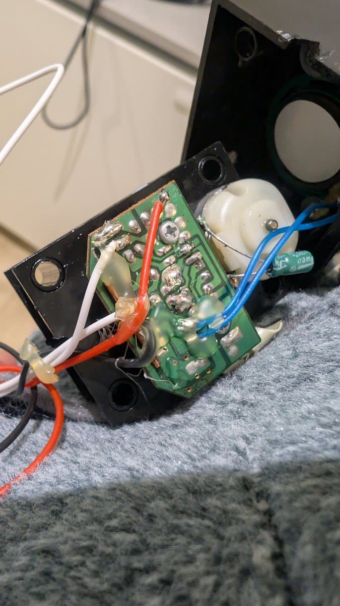 Green PCB with soldered components, white and blue wires, red and white connectors visible in black plastic housing during Totoro toy repair.