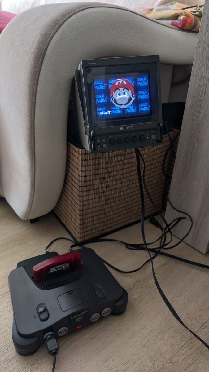 Nintendo 64 console with controller and red blower, connected to Sony monitor displaying Super Mario 64 title screen during recap repair.
