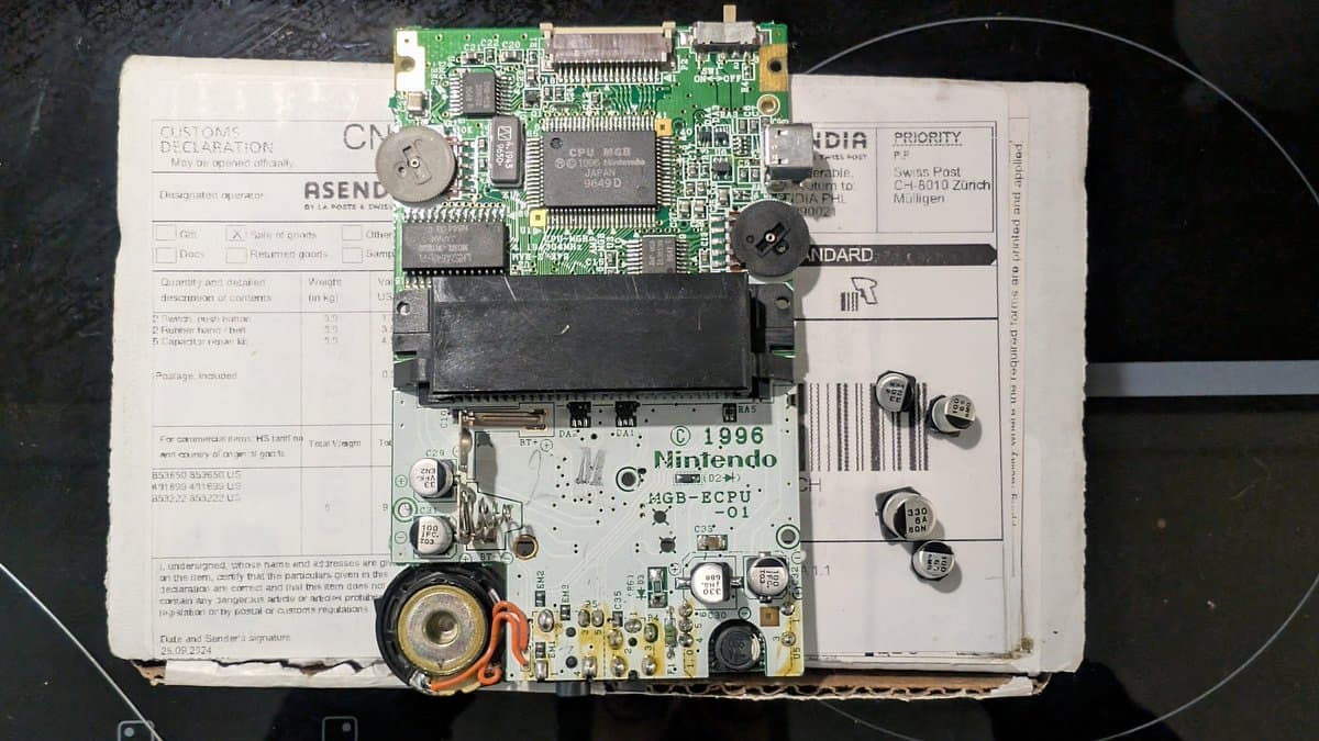 Game Boy Pocket motherboard with removed CPU board, exposed capacitors, potentiometers, and power components during restoration work.