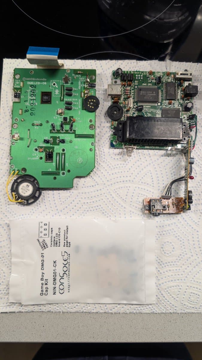 Nintendo DMG Game Boy PCBs during recap repair: green mainboard with new capacitors installed, donor board right, service card visible below.
