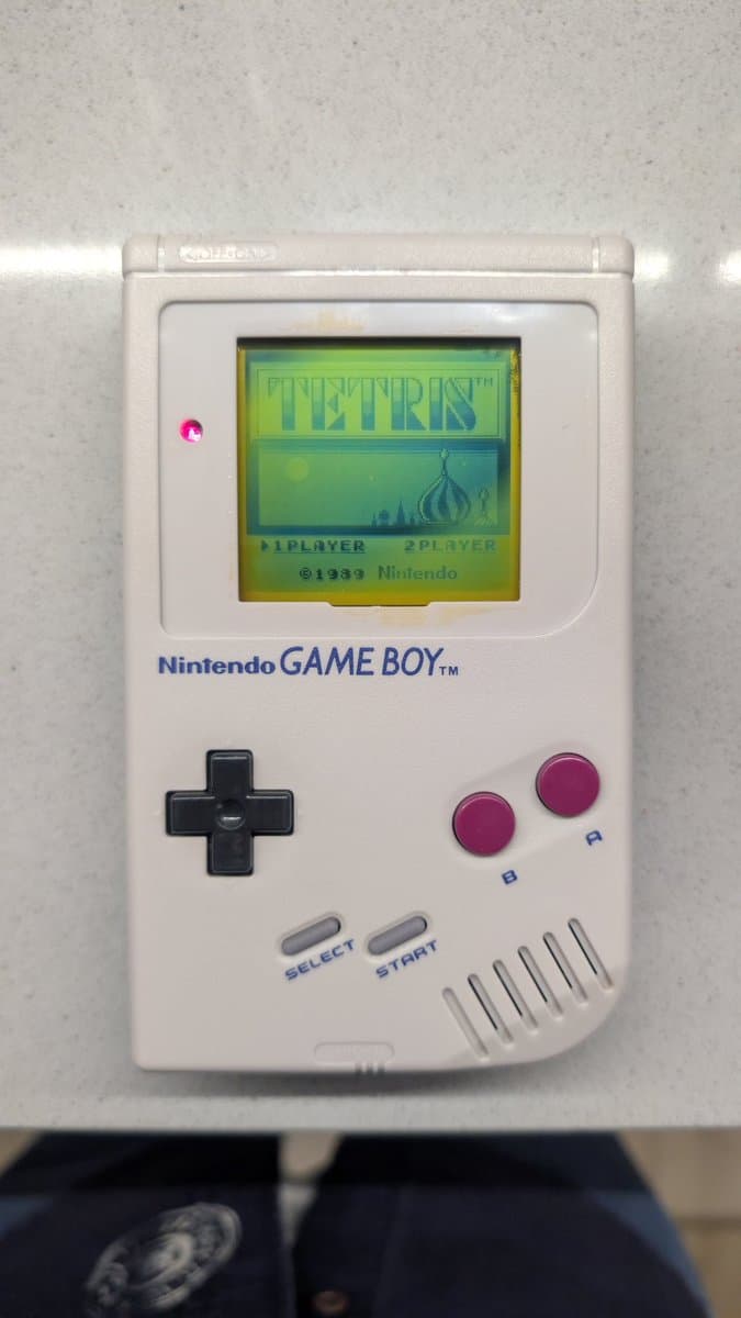 Nintendo Game Boy DMG displaying Tetris after recap service; less yellowed cream shell, working screen, magenta buttons visible.