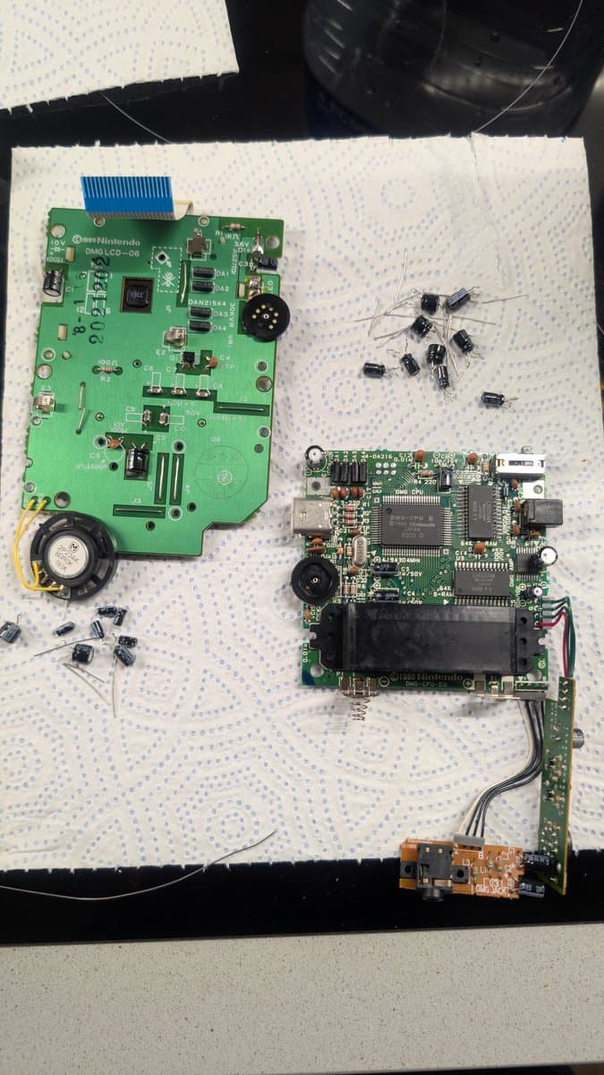 Nintendo DMG Game Boy mainboard during recap repair, with removed capacitors and a logic board displaying solder joints and IC chips.