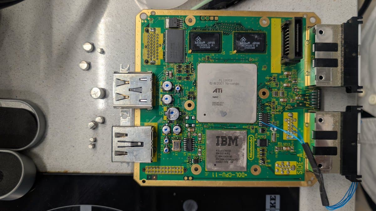 GameCube motherboard with ATI GPU and IBM processor visible; fresh capacitors installed on optical drive board during restoration.