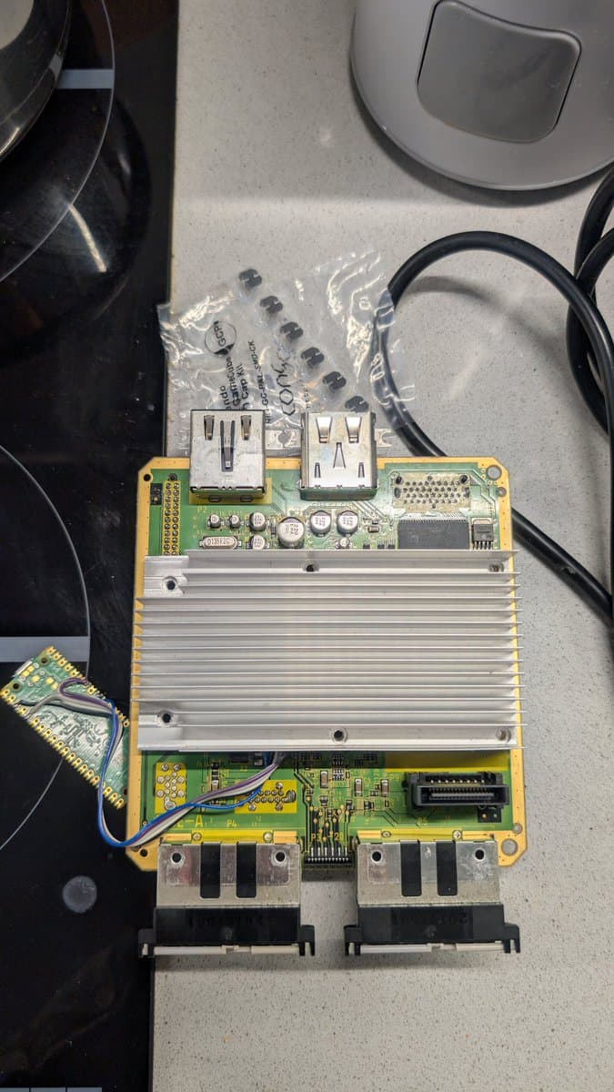 Disassembled GameCube motherboard with recapped power supply unit, dual heatsinks, and replacement capacitors visible during restoration work.