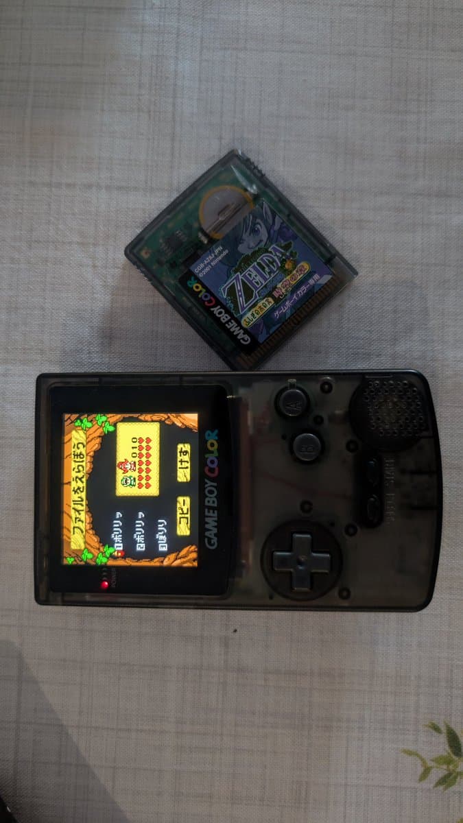 Game Boy Color with Zelda game displayed, cartridge above showing fresh battery installation for save data backup and restoration.