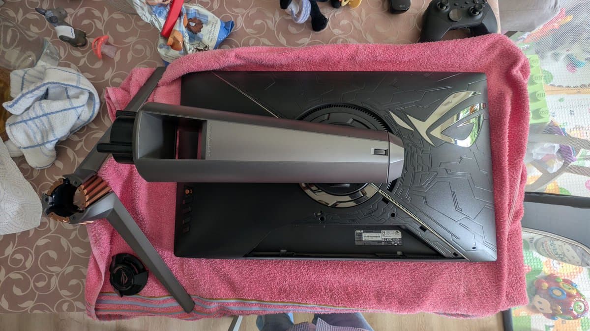 Asus PG27UQ monitor disassembled on pink towel, exposing internal fan and heatsink during refurbishment maintenance.