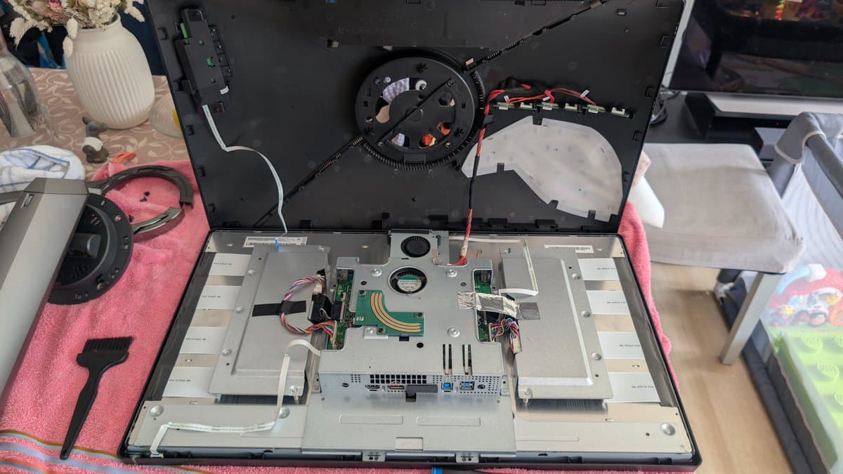 Asus PG27UQ monitor disassembled, exposing mainboard with new capacitors, fan replacement in progress, pink work mat with tools.