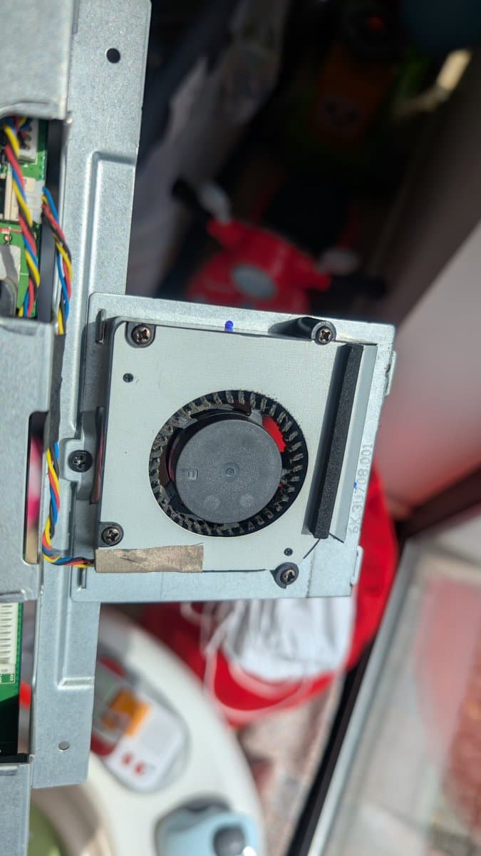 Disassembled cooling fan with visible dust buildup and dried thermal paste residue on mounting bracket; colorful wire connectors visible on adjacent PCB.