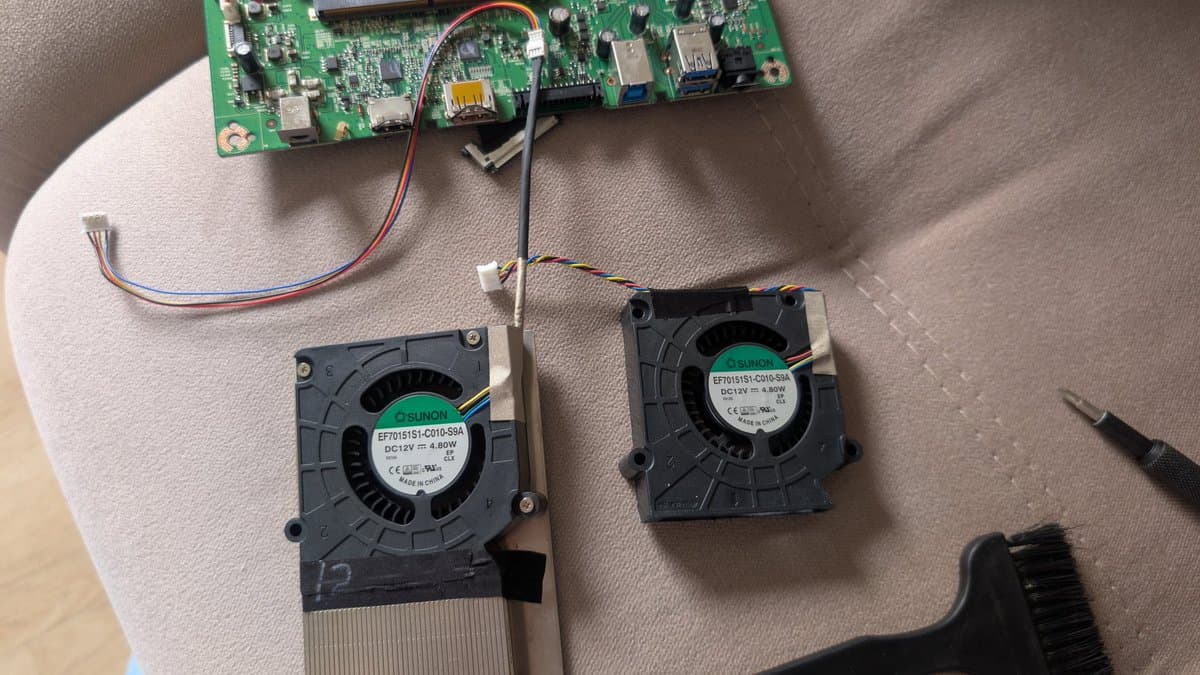 Two replacement cooling fans for Asus PG27UQ monitor next to mainboard with wiring harnesses during refurbishment.