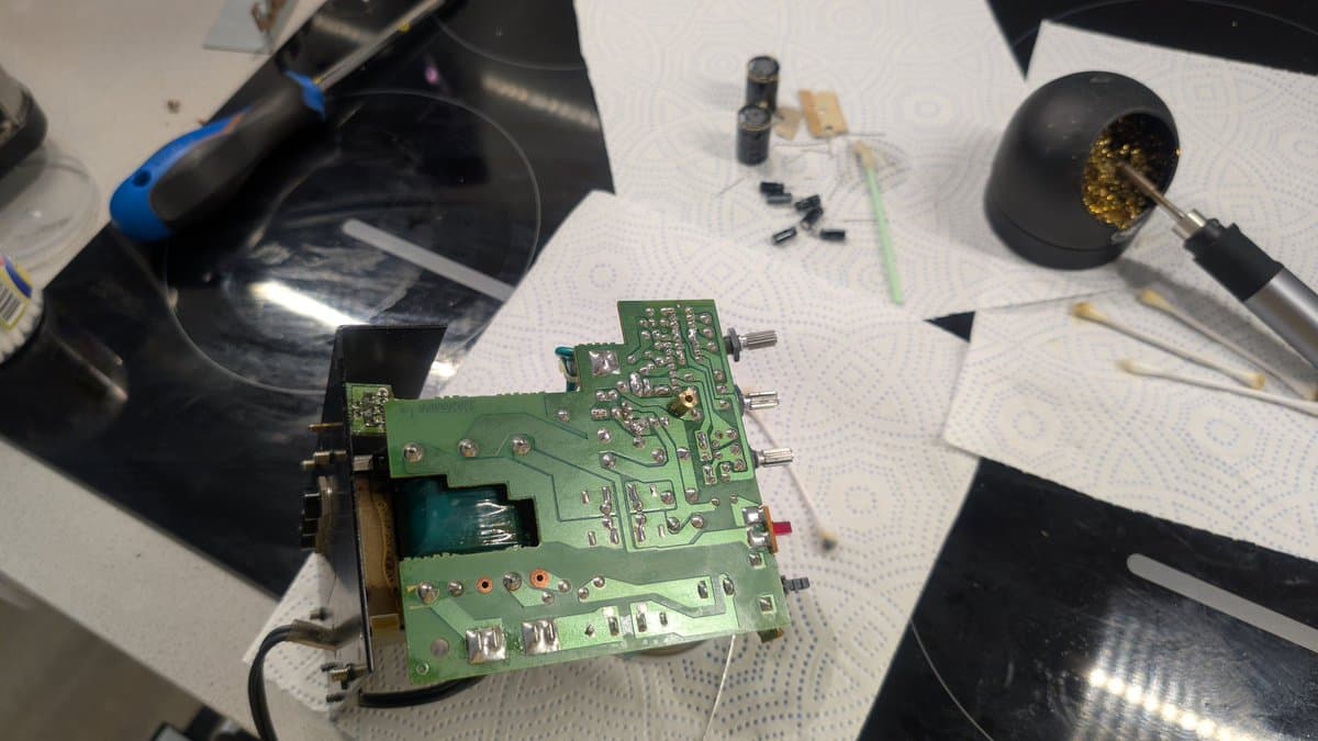 BOSS MA-12AV amplifier PCB during repair with soldering iron, capacitors, and electronic components on workbench.