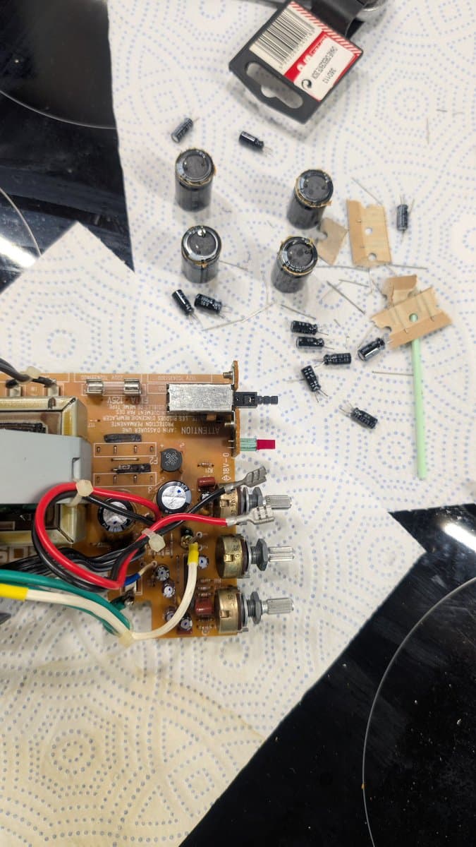 Disassembled BOSS MA-12AV amplifier board with electrolytic capacitors, resistors, and transistors arranged for inspection and replacement during refurbishment.