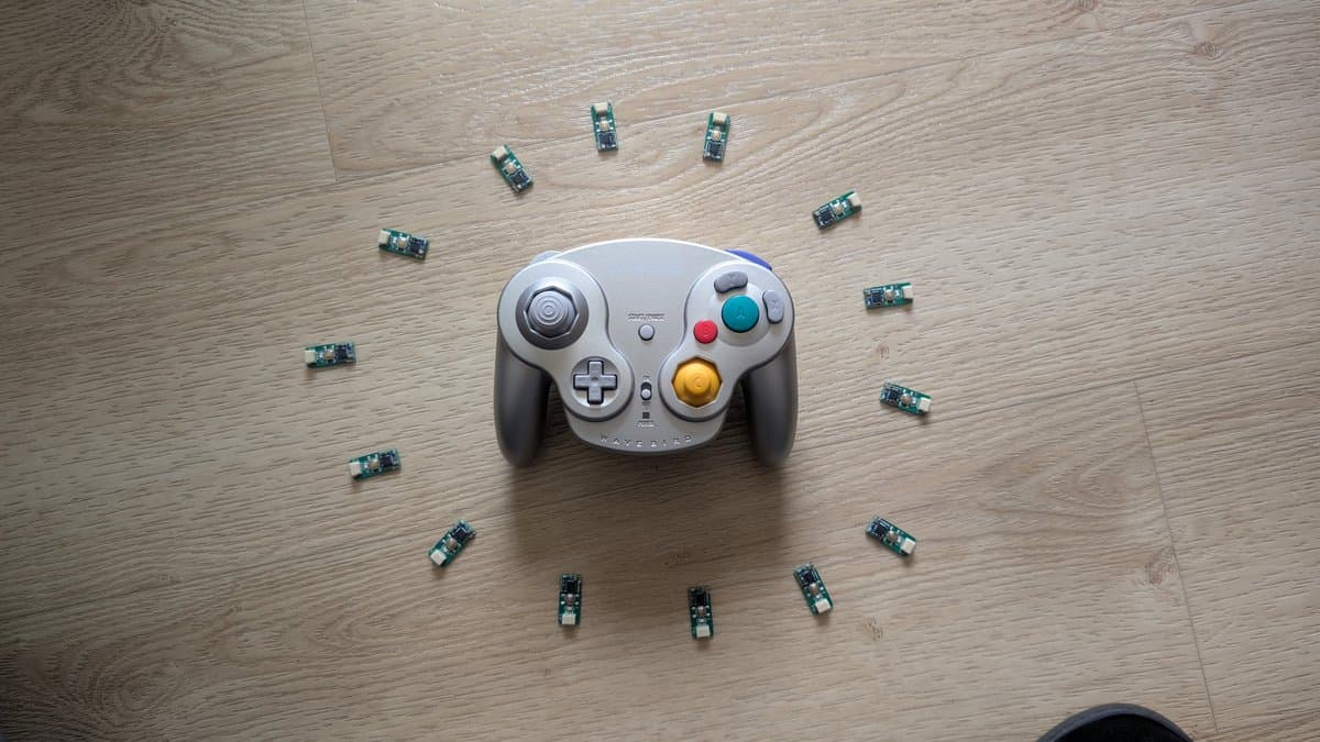 GameCube WaveBird controller surrounded by twelve WavePhoenix receiver PCBs arranged in a circle on wooden surface.