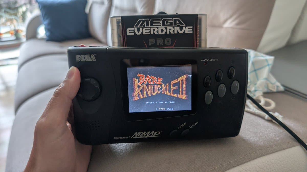 Sega Genesis Nomad handheld with Mega Everdrive Pro cartridge inserted, displaying Bare Knuckled title screen after restoration and USB power mod.