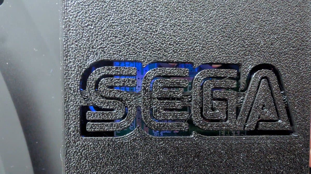 Close-up of Sega Nomad embossed logo on textured black plastic casing, showing metallic raised lettering with blue iridescent reflection.