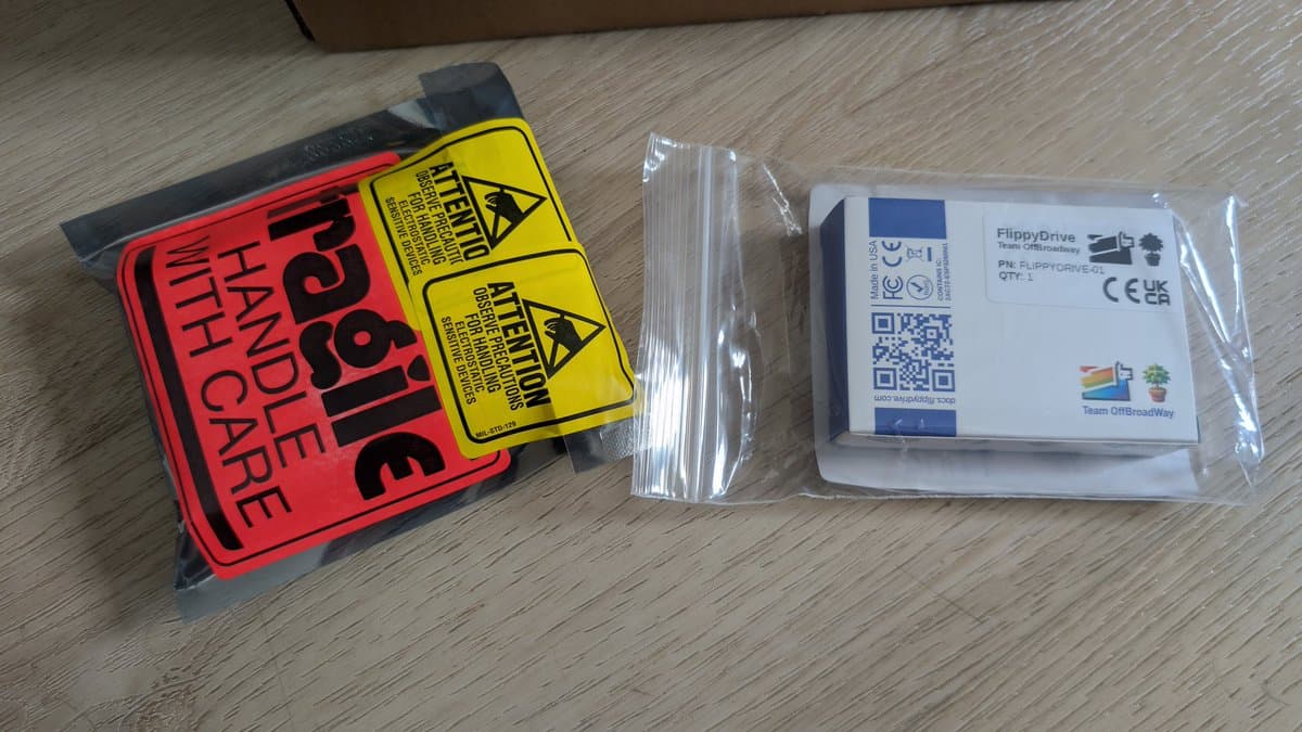 FlippyDrive optical drive replacement unit and static warning labels on wooden workbench during GameCube restoration.