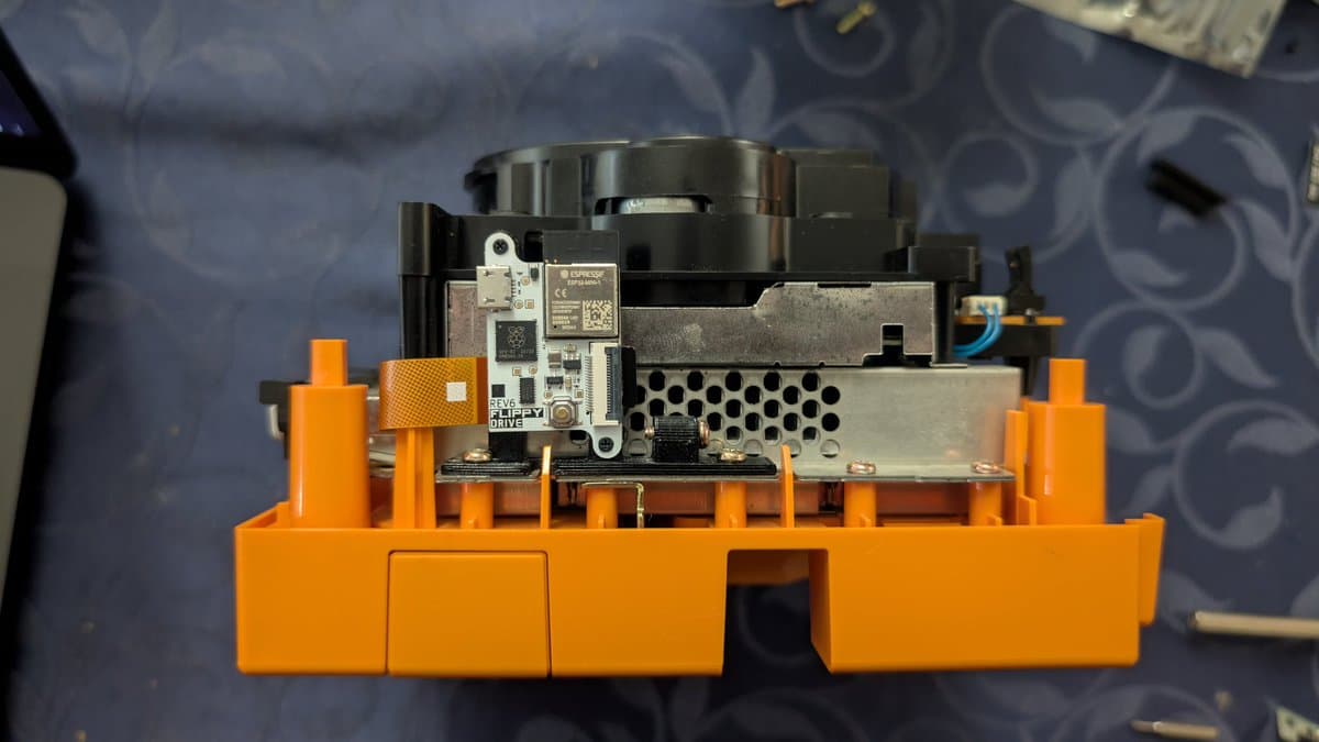 Disassembled orange GameCube motherboard with Picoboot and FlippyDrive components visible, showing internal electronics and orange plastic chassis.