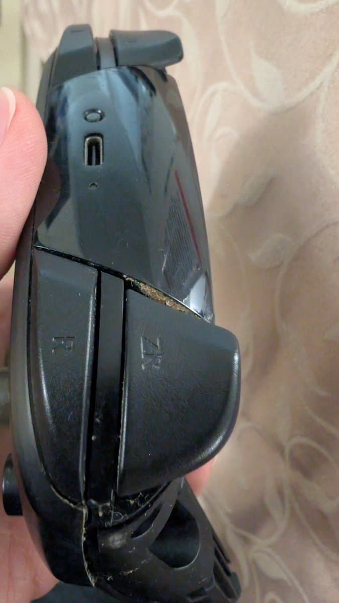 Nintendo Switch Pro controller held in hand showing wear damage, dirt accumulation, and separation along the seam requiring cleaning and maintenance.