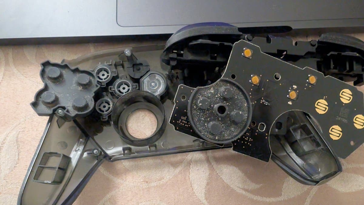 Disassembled Switch Pro controller showing dusty PCB board with gold contact pads and corroded internal components during cleaning maintenance.