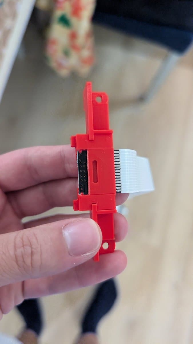 Red 3D-printed SD card extender adapter for 3DO ODE, showing connector pins and white ribbon cable, held in hand during installation.