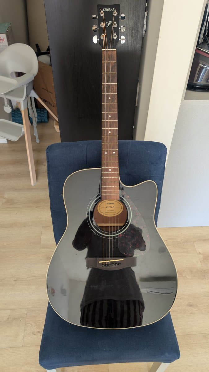 Yamaha FX370C acoustic guitar on blue chair showing cleaned fretboard, polished body, and new strings after maintenance.