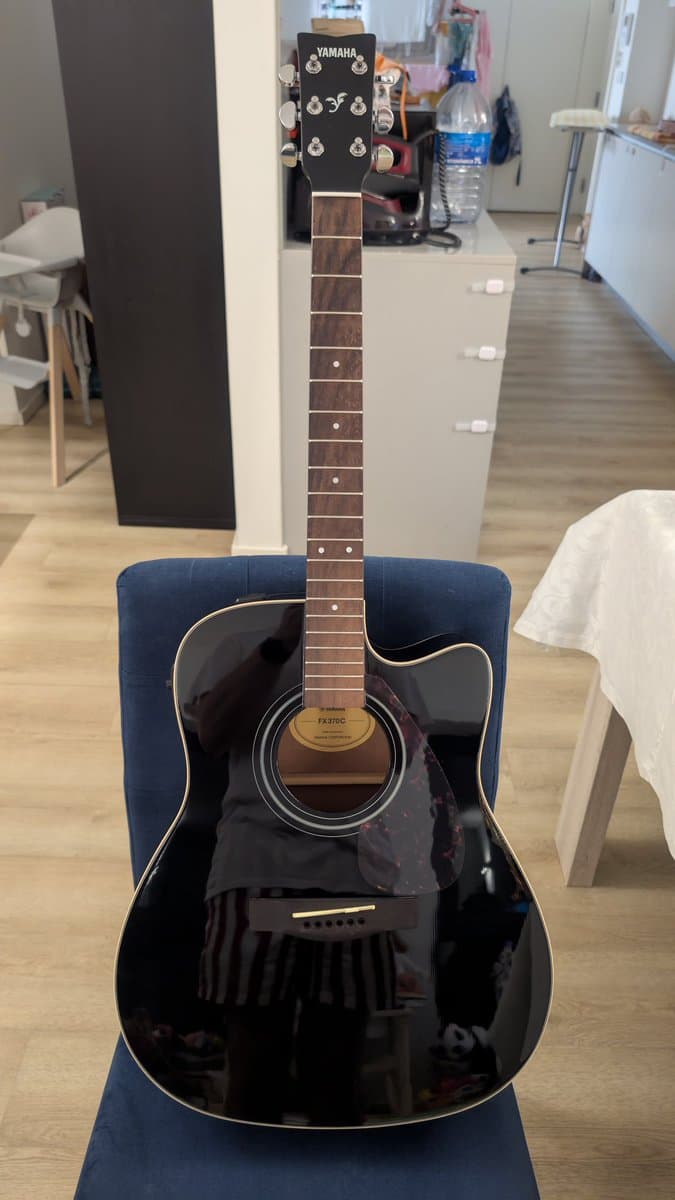 Yamaha FX370C acoustic guitar with black finish resting on blue stand, showing fretboard and headstock with tuning pegs during maintenance.