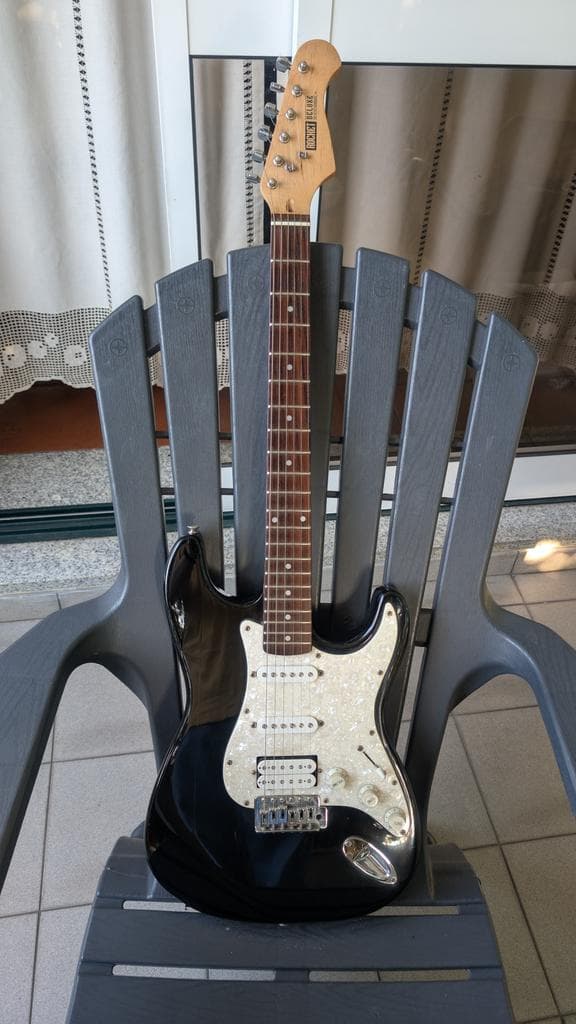 Black Fender Stratocaster with cream pickguard on stand, displaying cleaned and polished finish after restoration work.