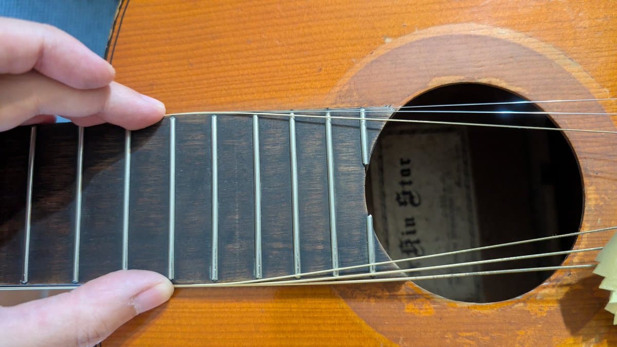 Close-up of acoustic guitar fretboard and strings showing cleaning and polishing work on frets and rosewood board.