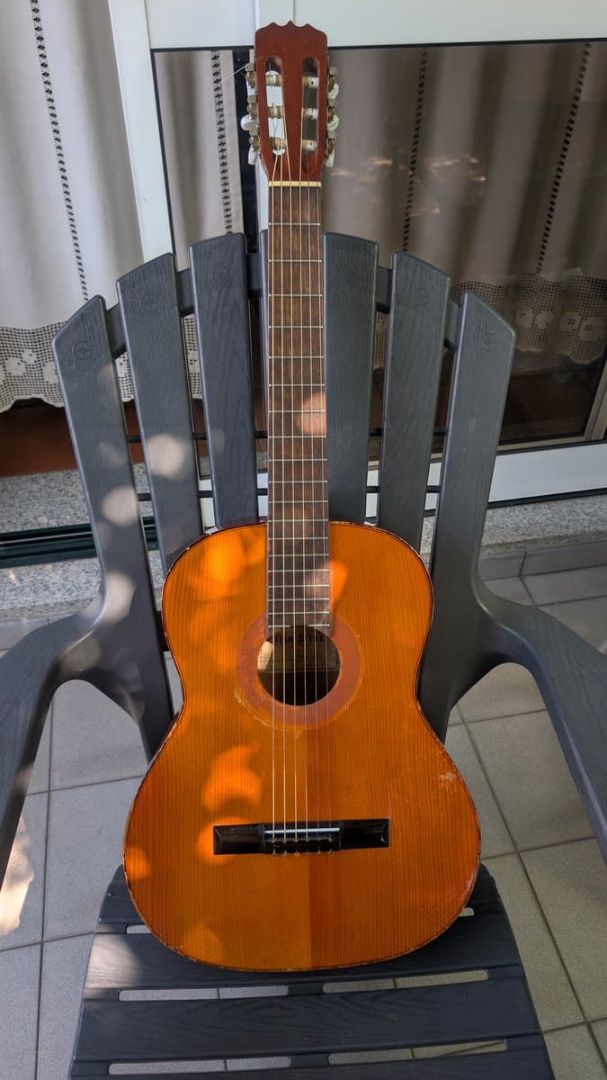 Classical acoustic guitar with polished orange-brown finish displayed on gray chair, showing cleaned frets and conditioned fretboard after restoration work.