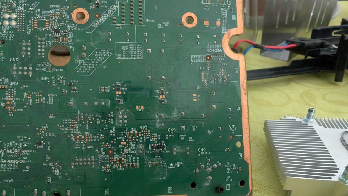 Xbox 360 E motherboard showing liquid damage residue, with heatsink removal in progress and power supply recap work visible.