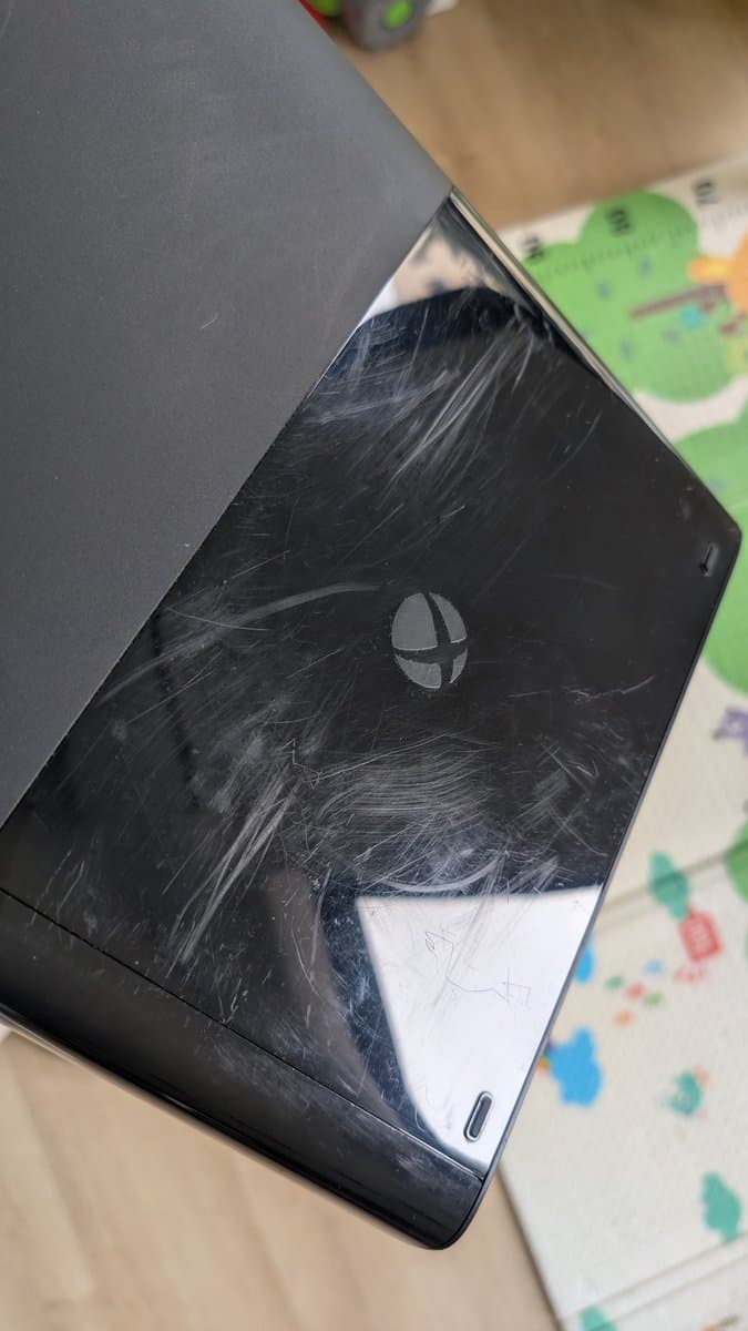 Xbox 360 E shell showing deep scratches and scuff marks on black casing during cleaning restoration.