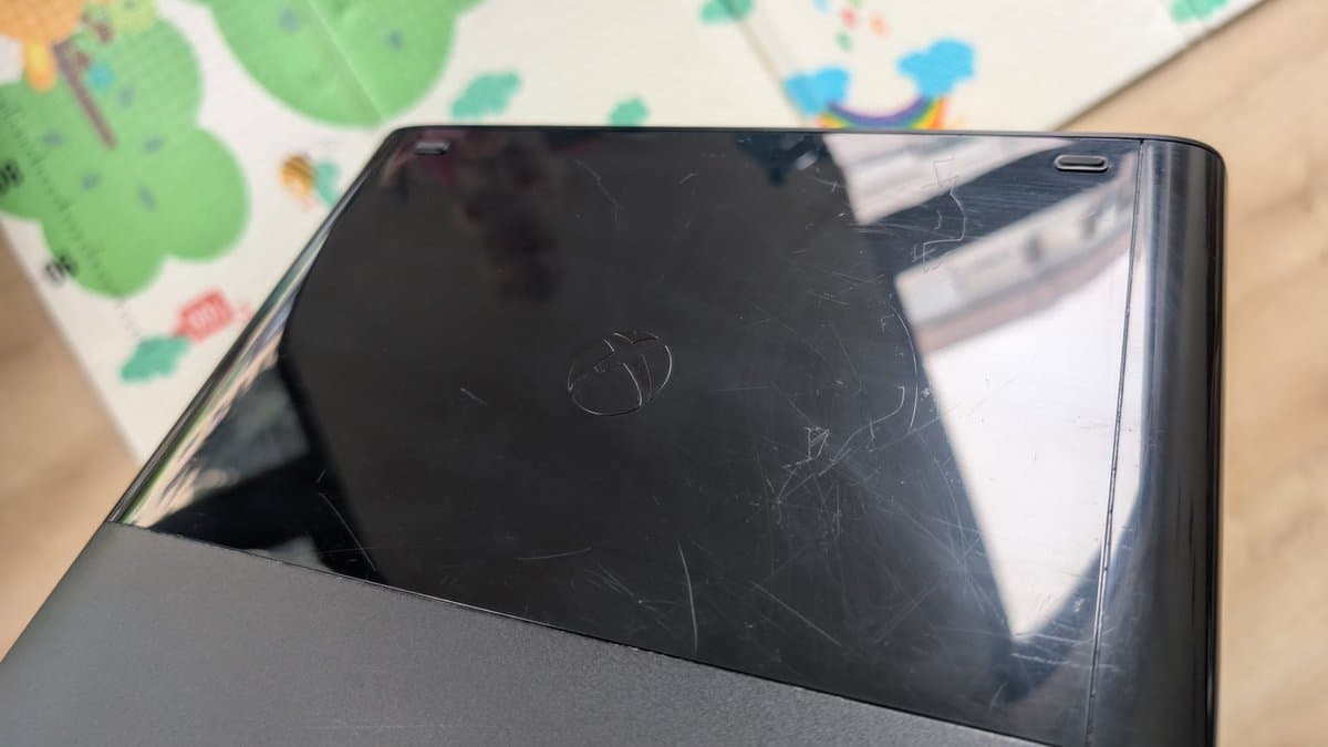 Xbox 360 E shell with heavy scratches and scuff marks on black plastic casing, polished with PlastX compound.