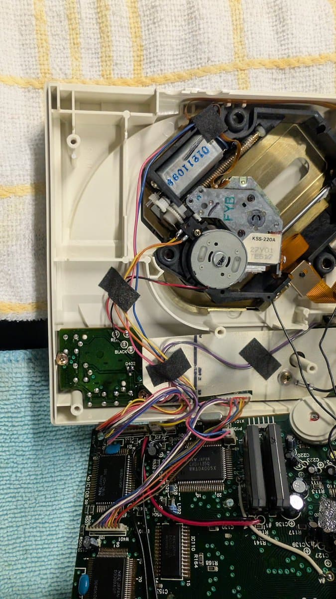 PC Engine CD-ROM2 internals exposed: motor assembly, laser mechanism, circuit boards, and wiring harness during laser swap repair work.