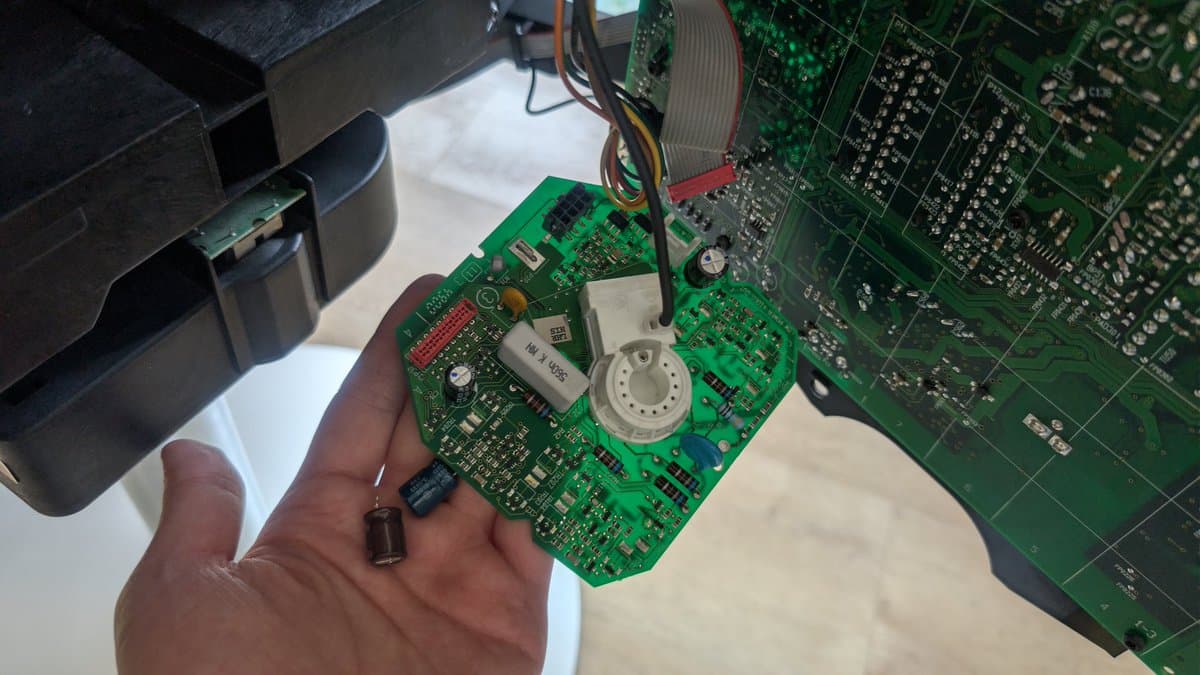 Technician holds recapped B&O Beovision 1 neck board showing reflowed solder joints and replaced X2 safety capacitor after smoke incident repair.