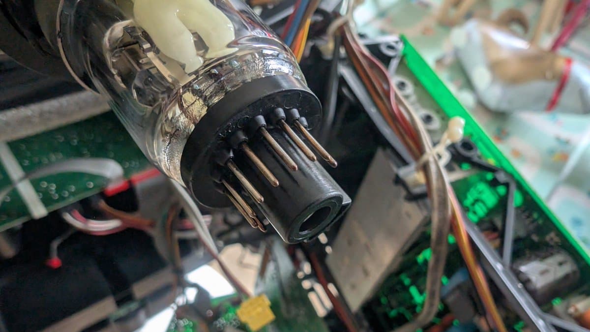 Close-up of corroded CRT connector pins being cleaned; X2 safety cap visible in background among circuit boards and wiring.