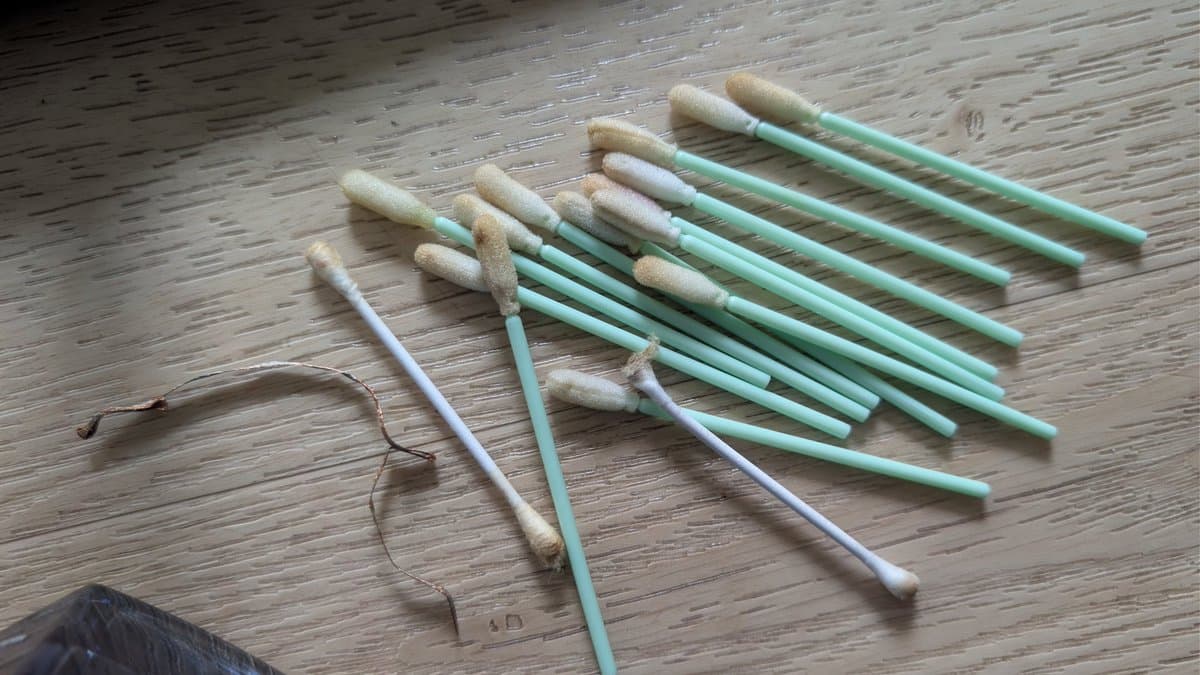 Charred debris and burnt capacitor remains laid out on wooden surface next to cleaning swabs and tools used for post-smoke cleanup.