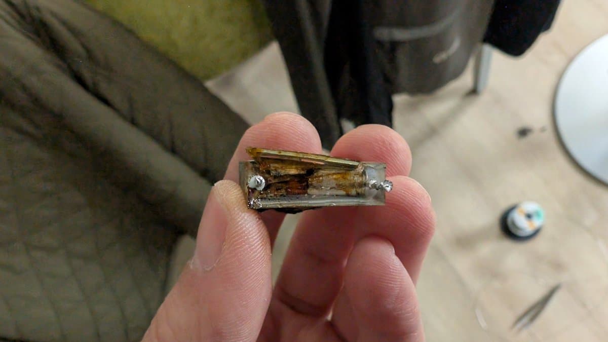 Burnt-out X2 safety capacitor held in fingers, showing catastrophic thermal damage and internal failure from the Beovision 1 repair.