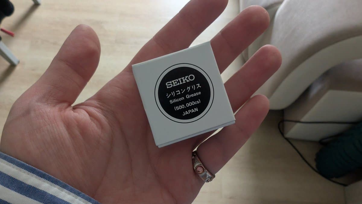 Hand holding small white box of Seiko Silicon Grease (500.000cs), Made in Japan, for watch maintenance and repair.