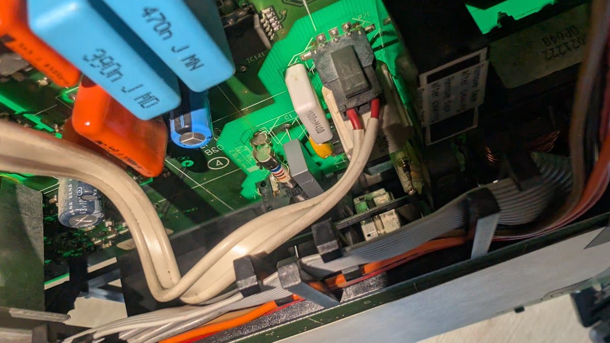 Closeup of B&O Beovision 1 green PCB showing replaced X2 safety capacitor, solder joints, and white cable routing during repair completion.